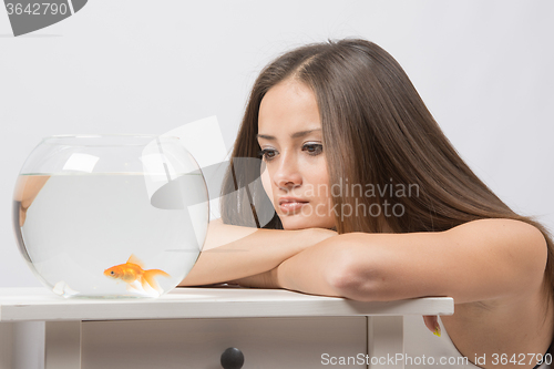 Image of Sad young girl looking with indifference at the little goldfish