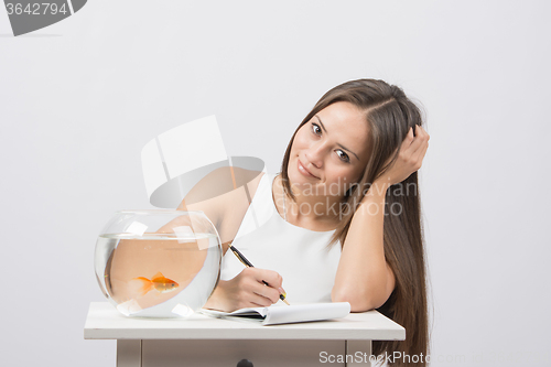 Image of Girl writing in a notebook, standing next to an aquarium with goldfish