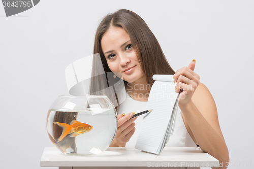 Image of Girl shows a pen in a notebook record gold fish in the aquarium
