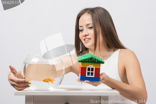 Image of She knocks on the wall of the aquarium with goldfish and the other hand holding a toy house