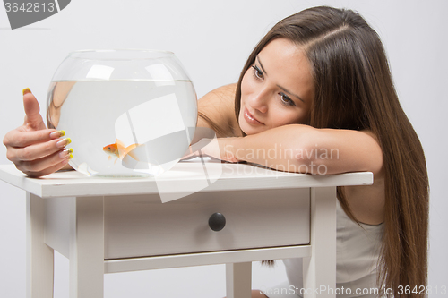 Image of The girl looks at a small goldfish in a fishbowl