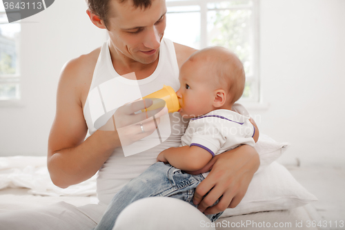 Image of Young father with his nine months old son on the bed at home