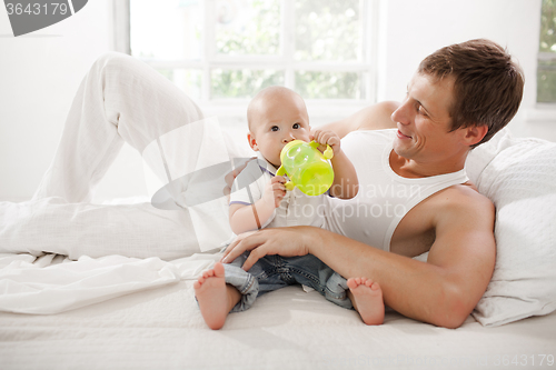 Image of Young father with his nine months old son on the bed at home