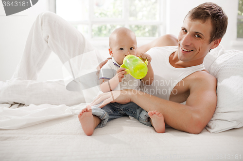 Image of Young father with his nine months old son on the bed at home