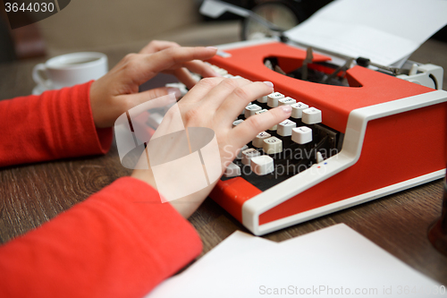 Image of human hands writing on red typewriter