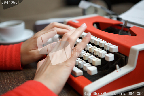 Image of human hands writing on red typewriter