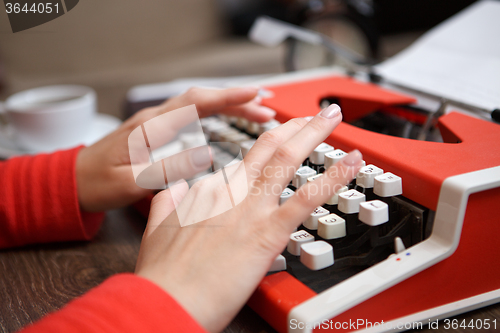 Image of human hands writing on red typewriter