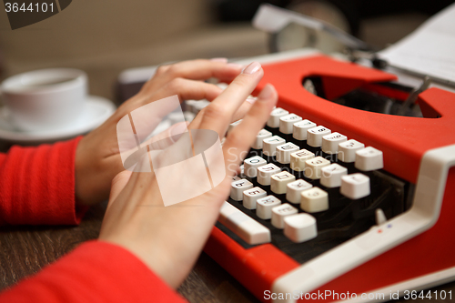 Image of human hands writing on red typewriter