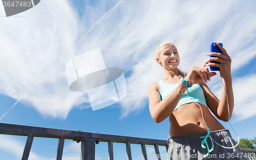 Image of happy woman with smartphone and earphones outdoors