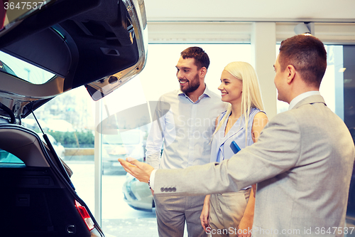 Image of happy couple with car dealer in auto show or salon