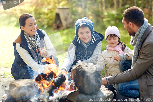 Image of happy family roasting marshmallow over campfire