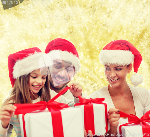 Image of happy family in santa hats sitting with gift boxes