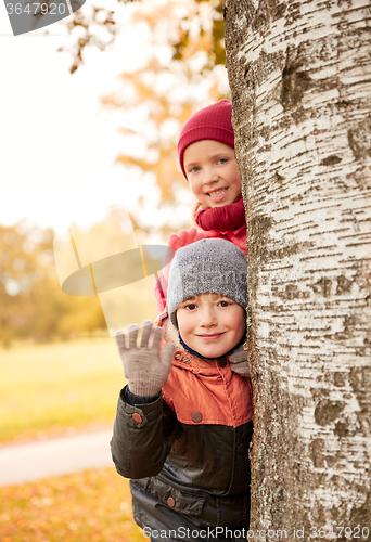 Image of happy children hiding behind tree and waving hand