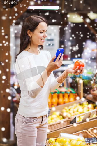 Image of happy woman with smartphone and tomato in market