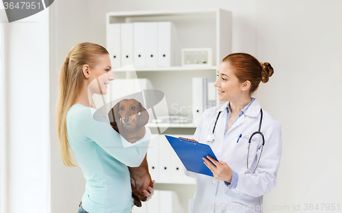 Image of happy woman with dog and doctor at vet clinic