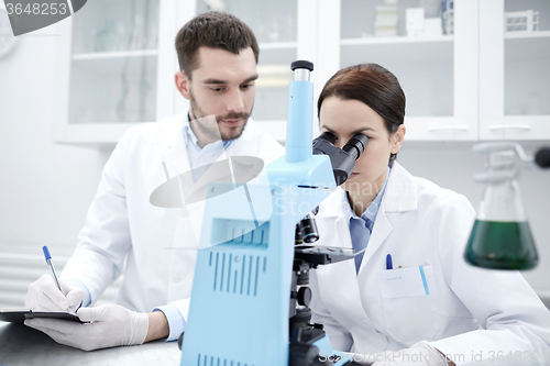 Image of scientists with clipboard and microscope in lab