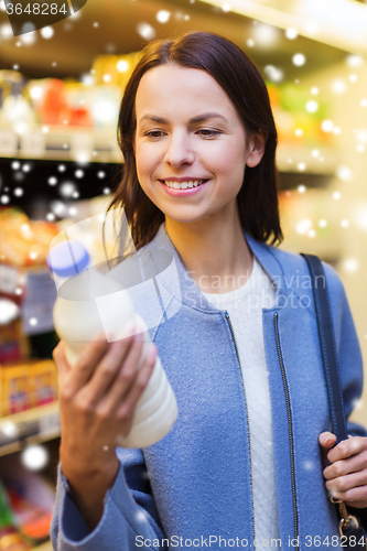 Image of happy woman holding milk bottle in market