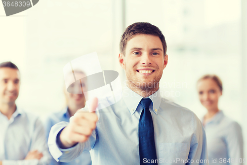 Image of smiling businessman showing thumbs up in office