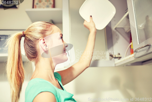 Image of happy woman putting plate to kitchen cabinet