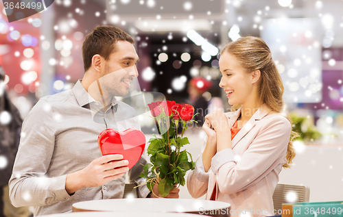 Image of happy couple with present and flowers in mall