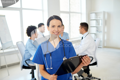 Image of happy doctor with clipboard over group of medics