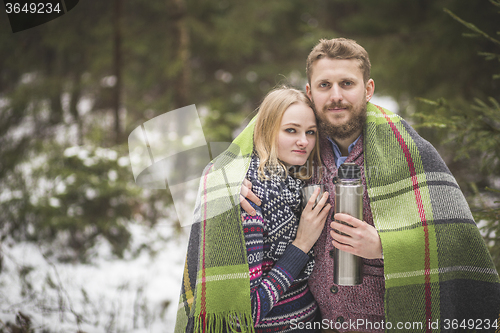 Image of Young couple in a warm blanket with thermos flask