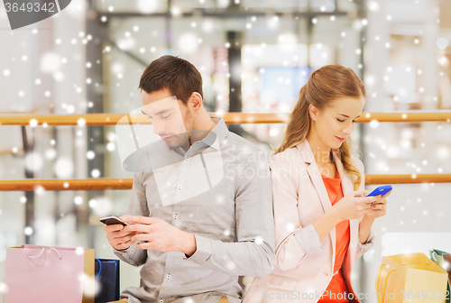 Image of couple with smartphones and shopping bags in mall