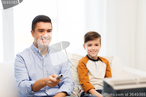 Image of smiling father and son watching tv at home