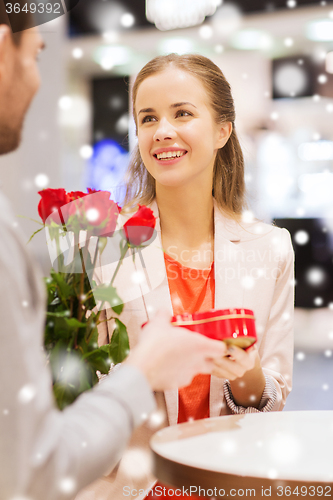 Image of happy couple with present and flowers in mall