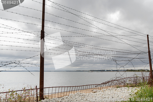 Image of barb wire fence over gray sky and sea