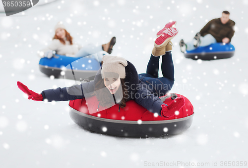 Image of group of happy friends sliding down on snow tubes