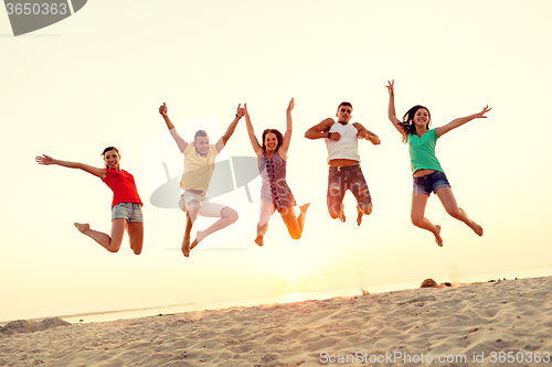 Image of smiling friends dancing and jumping on beach