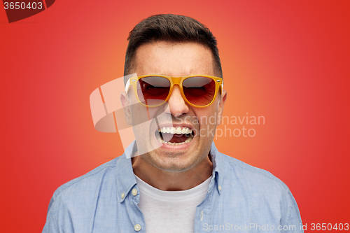 Image of face of angry man in shirt and sunglasses over red