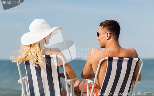 Image of happy couple sunbathing in chairs on summer beach