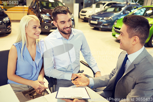 Image of happy couple with car dealer in auto show or salon