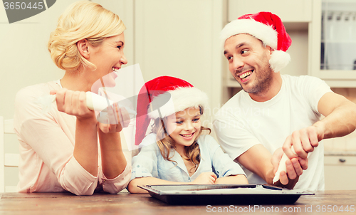 Image of happy family in santa helper hats making cookies