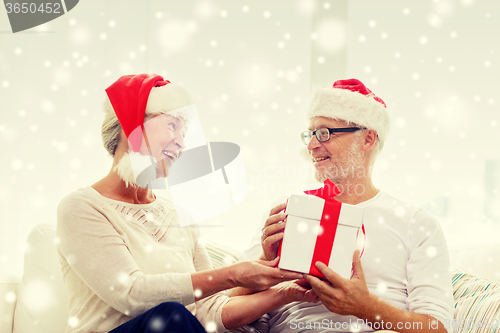 Image of happy senior couple in santa hats with gift box