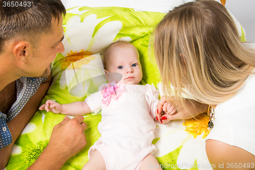 Image of Mom and dad are looking at a two-month baby who is lying on the bed