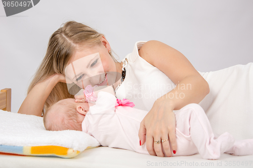 Image of Mom lovingly watching her baby lying on the bed with him