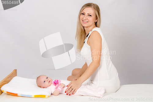 Image of Happy mother sitting on a bed at his two-month daughter and looks in the picture