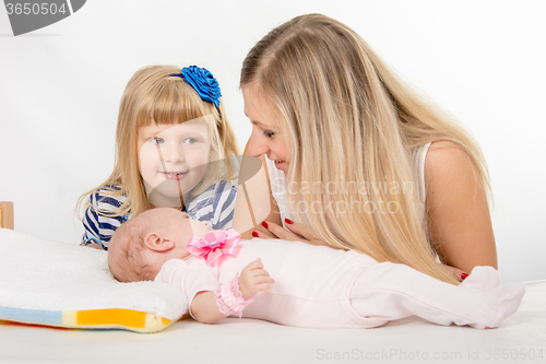 Image of The five-year girl is looking at her mother who is looking at newborn daughter