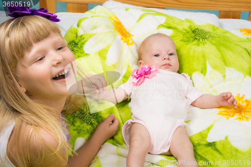 Image of Five-year girl joyfully laughs while holding the handle of a newborn baby