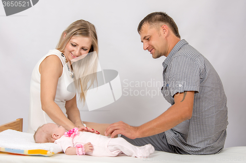 Image of Mom and dad sit on the bed on which lay their baby