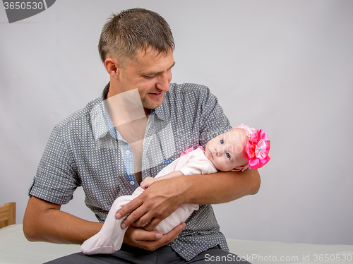 Image of Joyful father holding newborn daughter and looks at her