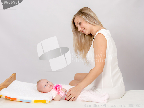 Image of Happy mother sitting on a bed and looking at a two-month daughter