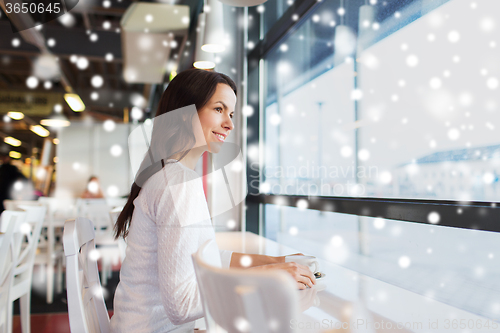 Image of smiling young woman drinking coffee at cafe