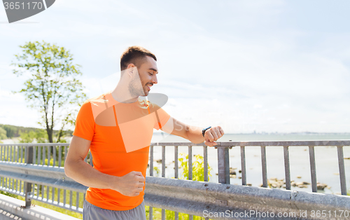 Image of smiling young man with smart wristwatch at seaside