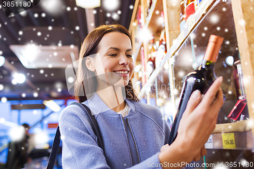 Image of happy woman choosing and buying wine in market