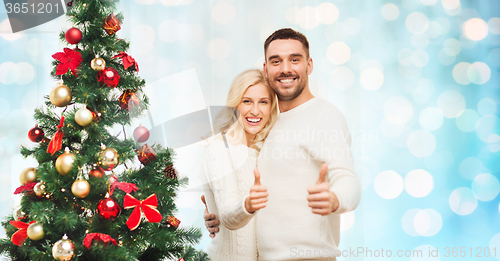Image of happy couple showing thumbs up with christmas tree