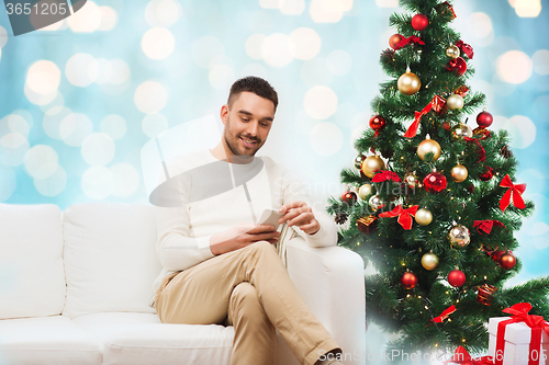 Image of smiling man with smartphone over christmas lights